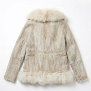 May include: A light-colored suede jacket with a fur collar and trim. The jacket features a textured pattern and a decorative band around the waist and hem. The fur trim is a creamy white color.