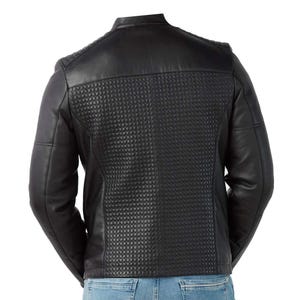 Op de afbeelding: Zwarte leren jas met een gewatteerd rugpaneel en schouderdetails. De jas heeft een klassieke kraag en lange mouwen. De achterkant heeft een gestructureerd, gewatteerd patroon. De jas wordt gedragen met een blauwe jeans.