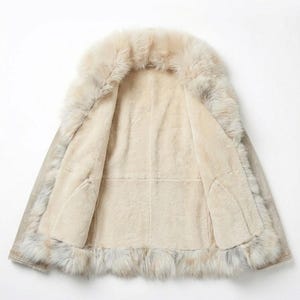 May include: Open view of a beige shearling coat with a fur collar and trim. The interior is a soft, light beige, and the exterior has a subtle, neutral tone. The fur trim adds a luxurious touch to this outerwear.