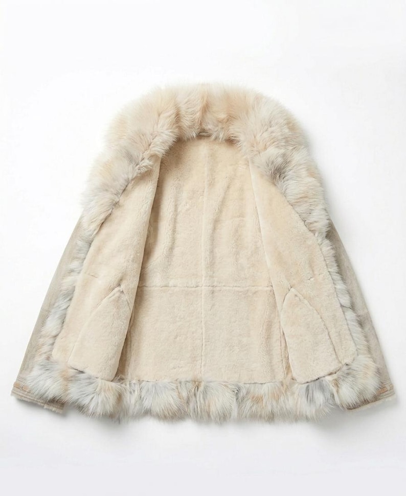 May include: Open view of a beige shearling coat with a fur collar and trim. The interior is a soft, light beige, and the exterior has a subtle, neutral tone. The fur trim adds a luxurious touch to this outerwear.