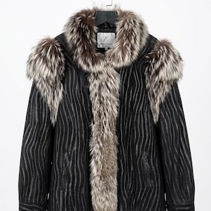 Puede incluir: Una chaqueta negra con un estampado de cebra, con cuello y adornos de piel. La chaqueta está colgada de una percha negra. El ribete de piel es una mezcla de marrón y plata.