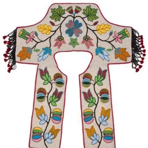 May include: Cream-coloured beaded garment with a floral design. The garment features a central floral motif with blue, yellow, and orange flowers, and green leaves. The edges are trimmed with a red border and black beaded fringe.