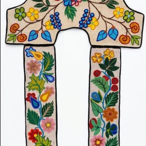 May include: An embroidered textile in beige, adorned with a vibrant floral pattern. The design incorporates red, blue, yellow, and orange flowers, green leaves, and blue berries. It has a black border and an unusual shape, possibly for decoration.