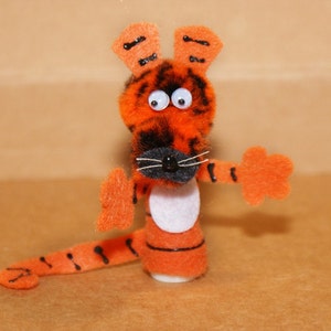 May include: Orange and black finger puppet of a tiger with white eyes and a white belly. The tiger has a black nose and whiskers.
