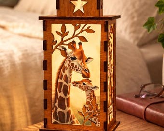 Op de afbeelding: Een rechthoekige houten lantaarnlamp met een lasergesneden ontwerp van een volwassen giraf en een kalf tussen boomtakken. Het bovenste gedeelte bevat een uitgesneden stervorm. De lamp verspreidt een warme, zachte gloed die de giraffescène verlicht.