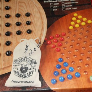 May include: A wooden Chinese Checkers game board with black, red, yellow, blue, and green marbles. A canvas bag with the text "RECREATIONAL WOODCRAFT" and "Channel Crafted Fun" is included. The game board is made of wood.