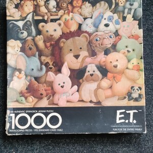 May include: A Springbok jigsaw puzzle featuring a colorful assortment of plush toy animals and characters, including E.T. The puzzle has 1000 interlocking pieces and fits a standard card table. The box has the text "FUN FOR THE ENTIRE FAMILY".