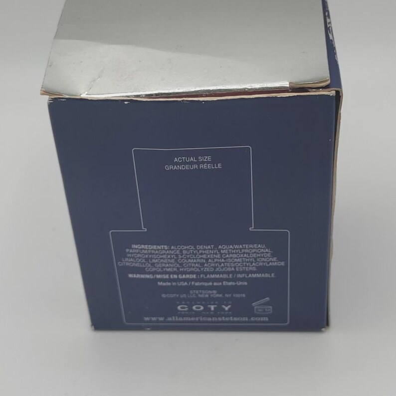 Peut inclure: Une bo&icirc;te de produit bleu marine avec du texte blanc, dont les mots "ACTUAL SIZE" et "GRANDEUR REELLE." La bo&icirc;te &eacute;num&egrave;re les ingr&eacute;dients et les avertissements. La marque "COTY" est visible en bas.