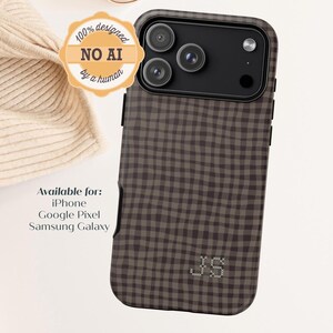 May include: A dark brown and light brown checkered phone case with a triple camera cutout and the initials JS embroidered in white cross-stitch at the bottom. Text on the image reads: 100% designed NO AI by a human. Available for: iPhone, Google Pixel, Samsung Galaxy.