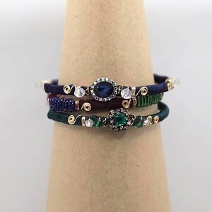 May include: A set of four bracelets with blue, green, and red silk thread, gold wire, and crystal and gemstone accents. The bracelets feature a blue oval-shaped gemstone and a green square-shaped gemstone.