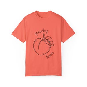 May include: A coral colored t-shirt with a black and white illustration of a peach and the text "spoochy keen".