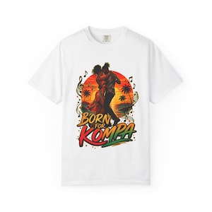May include: White t-shirt featuring a colorful graphic of a couple dancing in front of a sunset with palm trees. The text "Born for Kompa" is displayed in a vibrant font, with musical notes surrounding the scene.