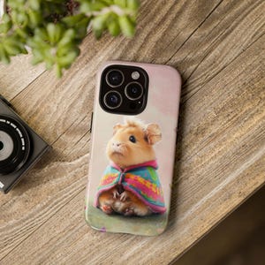 Könnte beinhalten: Eine Handyhülle mit einem niedlichen Cartoon-Hamster, der einen rosa-blauen Umhang trägt. Der Hintergrund ist zartrosa mit einer weißen Wolke.