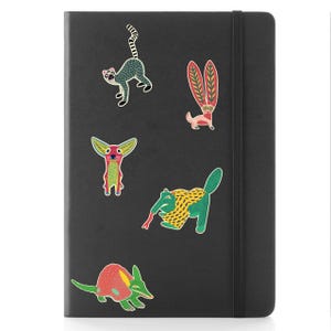 May include: A black notebook with a matching elastic closure and several colorful animal stickers. The stickers include a lemur, a dog-like creature, and an anteater. The notebook is a standard size.