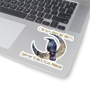 Könnte beinhalten: Ein Aufkleber mit einem schwarzen Raben, der auf einem goldenen Halbmond sitzt. Der Text "Crows Before Bros" und "Support Your Local Murder" ist in goldenen Buchstaben geschrieben.