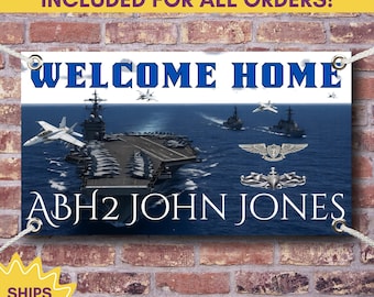 May include: A navy blue banner with the words "WELCOME HOME" in white. The banner features an image of an aircraft carrier, fighter jets, and ships at sea. The name "ABH2 JOHN JONES" is also displayed. The banner is hanging on a brick wall.