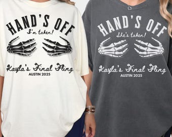 May include: Two oversized t-shirts, one cream and one charcoal gray, with the text "HAND'S OFF" and a skeleton hand graphic. The text "I'm taken!" and "She's taken!" are included. Below is "Kayla's Final Fling, Austin 2025."