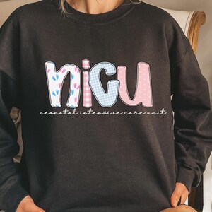 Op de afbeelding: Zwart sweatshirt met de letters "NICU" in een kleurrijk ontwerp. De "N" heeft blauwe en roze babyvoetjes, de "I" is een blauw ruitpatroon, de "C" is een roze ruitpatroon en de "U" is roze. De woorden "neonatal intensive care unit" staan eronder.