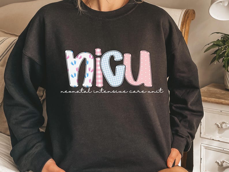 Op de afbeelding: Zwart sweatshirt met de letters "NICU" in een kleurrijk ontwerp. De "N" heeft blauwe en roze babyvoetjes, de "I" is een blauw ruitpatroon, de "C" is een roze ruitpatroon en de "U" is roze. De woorden "neonatal intensive care unit" staan eronder.
