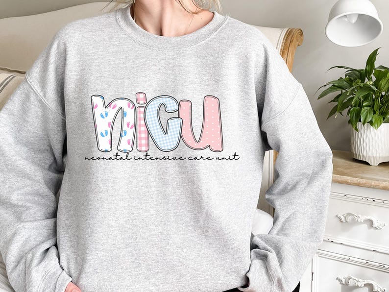 Op de afbeelding: Een lichtgrijs sweatshirt met de letters "NICU" in een kleurrijk ontwerp. De "N" heeft babyvoetjes, de "I" heeft een roze en wit geruit patroon, de "C" heeft een blauw en wit geruit patroon en de "U" heeft een roze stippenpatroon. Daaronder staat de tekst "neonatal intensive care unit".