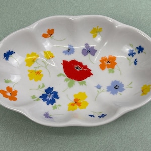 May include: White, scalloped-edge serving dish decorated with colorful floral patterns. The flowers are in shades of red, orange, yellow, blue, and purple. The dish has a cloud-like shape and is likely made of ceramic.
