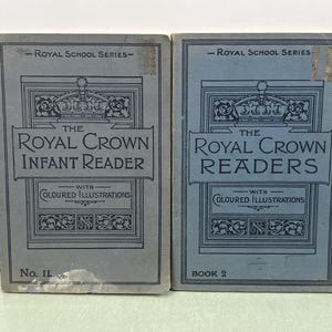 Puede incluir: Se muestran dos libros antiguos, "The Royal Crown Infant Reader" y "The Royal Crown Readers". Ambos libros tienen una cubierta azul grisácea con texto adornado y las palabras "Royal School Series". El Infant Reader está marcado "No. II" y el otro "Book 2".