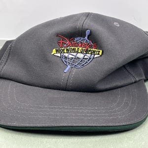 May include: Gray baseball cap with a curved brim and a green underside. The cap features an embroidered logo with the text "Disney's Wide World of Sports" in red, yellow, and blue.