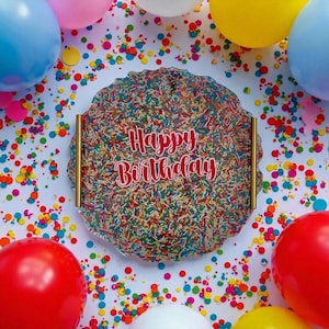 May include: A clear, round tray with a colorful sprinkle design and the words "Happy Birthday" in red script. The tray is surrounded by colorful confetti and balloons in red, blue, pink, and yellow.