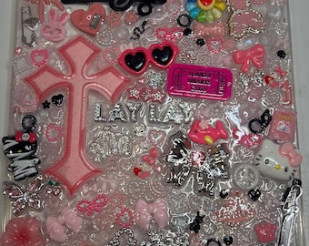 May include: A clear tablet case decorated with various pink and white charms, including Hello Kitty figures, a large pink cross, a glittery pink guitar, bows, hearts, and text reading a lil bougie, LAY LAY, and Queen, along with a pink Lonely Hearts Club ticket.