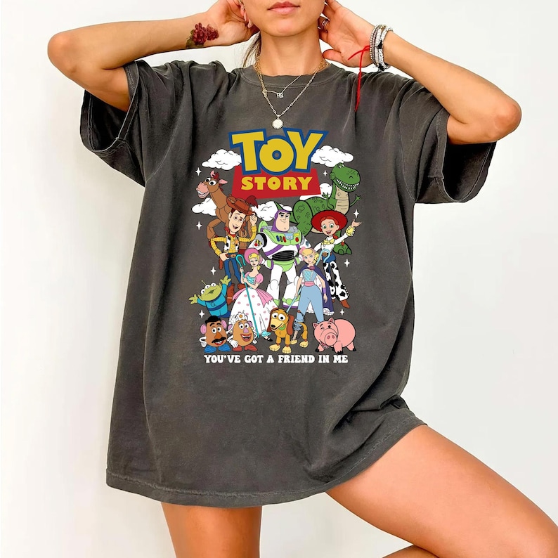 Op de afbeelding: Donkergrijs T-shirt met een kleurrijke afbeelding van personages uit de film "Toy Story". Het ontwerp bevat de titel van de film en de zin "You've got a friend in me".