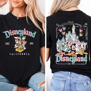 May include: Black t-shirt featuring the Disneyland logo in teal, pink, and yellow, with a group of cartoon characters. The front of the shirt says "Disneyland EST 1955 CALIFORNIA". The back of the shirt features a castle and more characters.