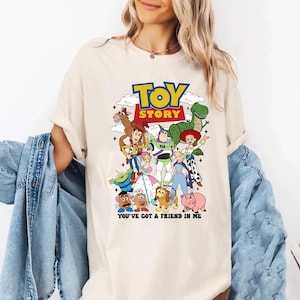 Op de afbeelding: Cr&egrave;mekleurig T-shirt met een kleurrijke afbeelding van personages uit de film "Toy Story". Het ontwerp bevat de titel van de film in geel en blauw, evenals de zin "You've Got a Friend in Me."