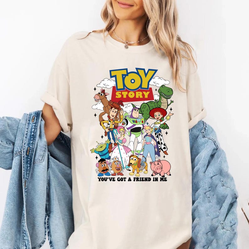 Op de afbeelding: Cr&egrave;mekleurig T-shirt met een kleurrijke afbeelding van personages uit de film "Toy Story". Het ontwerp bevat de titel van de film in geel en blauw, evenals de zin "You've Got a Friend in Me."