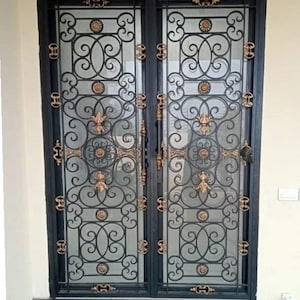 Puede incluir: Un par de puertas dobles de hierro forjado negro con intrincados diseños de volutas doradas. Las puertas tienen paneles de vidrio y están enmarcadas en negro.