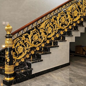 May include: A staircase featuring black marble steps and a decorative railing with intricate gold-coloured metal scrollwork and floral motifs. The railing includes a prominent black and gold newel post and a smooth wooden handrail along the top edge.