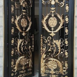 May include: A set of double doors made of black metal with intricate gold-coloured scrollwork and floral motifs. The arched doors feature symmetrical patterns, vertical bars, and decorative circular medallions, with gold handles on each door panel.
