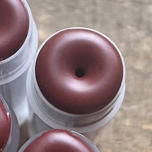 Puede incluir: Cuatro tubos de bálsamo labial marrones con un agujero en el centro de cada bálsamo. Los tubos son de plástico transparente.