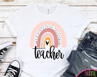 May include: White t-shirt with a pink, orange, and yellow rainbow design and the word "teacher" printed below. The rainbow has black polka dots and a small heart in the center.
