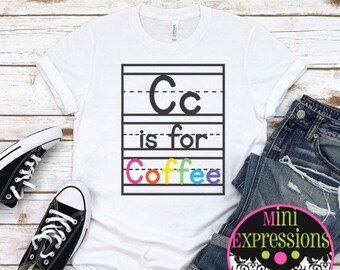 May include: White t-shirt with a black and white graphic that says "Cc is for Coffee". The graphic is in a school-style handwriting font with a rainbow colored "Coffee".