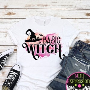 May include: White t-shirt with the words "Basic Witch" in black script, a witch hat graphic, and a pink watercolor background. The shirt is paired with blue jeans and black sneakers.