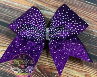 May include: Purple cheer bow with iridescent rhinestones and a black base. The bow is decorated with a gradient of purple glitter and rhinestones.