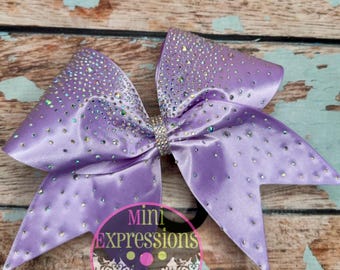 May include: A large purple cheer bow with iridescent rhinestones. The bow is made of satin and has a double loop design.