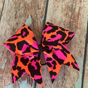 May include: A large pink and orange cheetah print cheer bow with a black elastic band.
