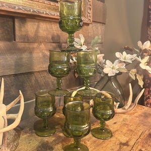 May include: A collection of vintage green glass goblets with a decorative pattern. The goblets are arranged in a pyramid shape, showcasing their unique design and color. The stemware is displayed on a wooden surface.