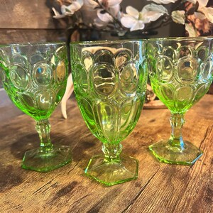 May include: Three green vintage goblets with a textured pattern. The goblets have a hexagonal base and a stem that leads to a round bowl. The goblets are made of glass and are a bright green color.
