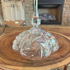 May include: A clear glass cloche with a cut crystal design and a tall, pointed finial. The cloche is sitting on a wooden surface.