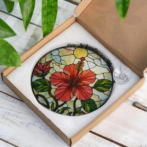 A stained glass flower in a cardboard box, with a clear glass piece inside the box.