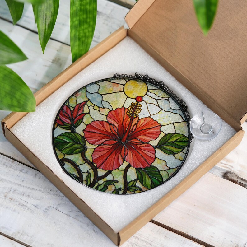 A stained glass flower in a cardboard box, with a clear glass piece inside the box.