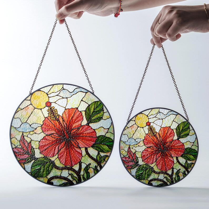 Two hands holding circular stained glass pieces featuring vibrant floral designs.