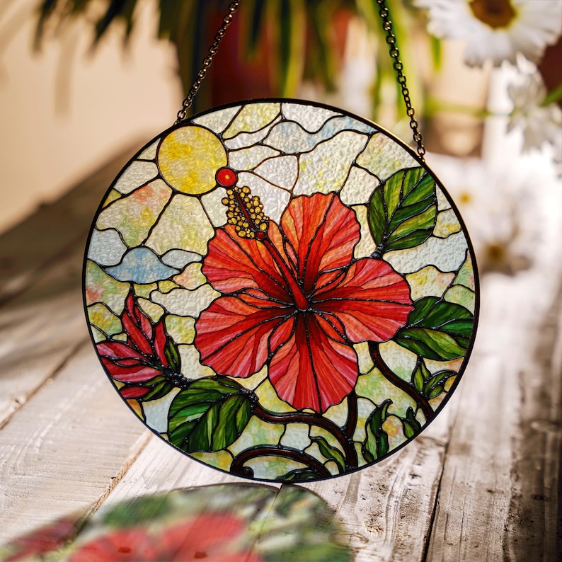 A stained glass window with a vibrant red hibiscus flower and green leaves, set against a cloudy sky background.